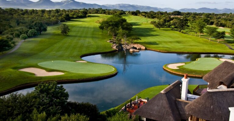 Aerial view of a golf course with green fairways, water hazards, and island greens, framed by trees and distant hills.