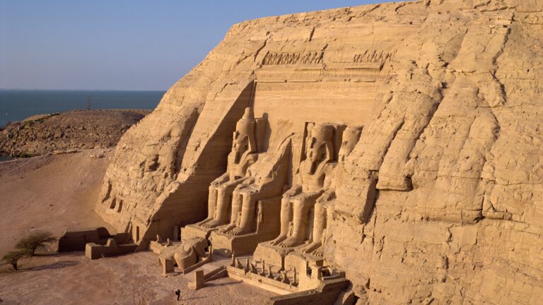 Abu Simbel temple facade carved into a sandstone cliff with four colossal Ramesses II statues at the entrance.