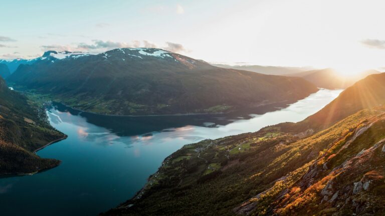 Sunset over a fjord bounded by towering green mountains and a winding valley below.