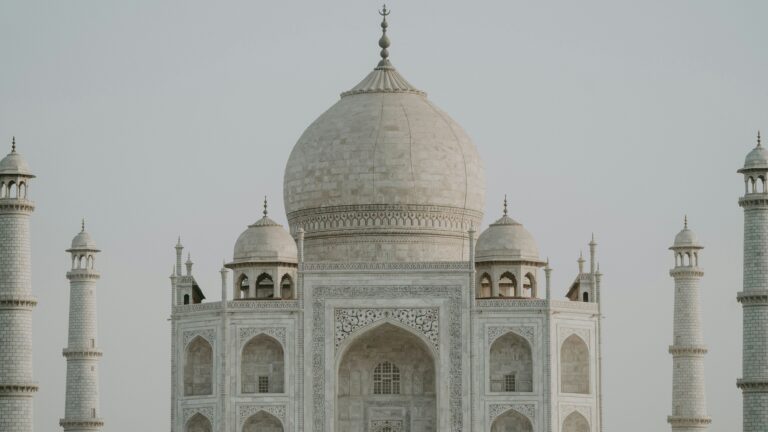 Front view of the Taj Mahal with its large central dome and four surrounding minarets against a pale sky.